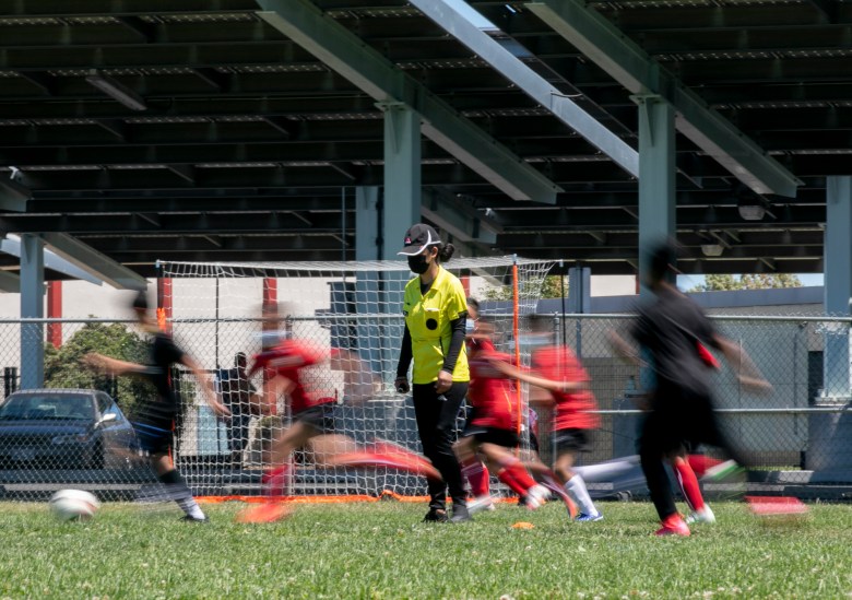 Players run past Claudeth as she referees a soccer game for a local children's league. Photo by Anne Wernikoff, CalMatters