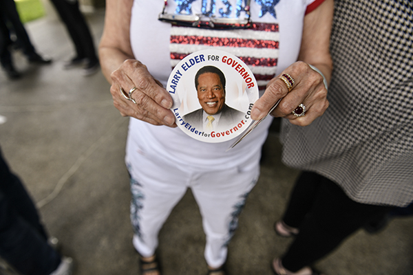 A supporter of conservative radio talk show host Larry Elder, holds a sticker in Norwalk, on July 13, 2021 during an event where Elder announced his bid as a recall candidate for governor. Photo by Pablo Unzueta for CalMatters