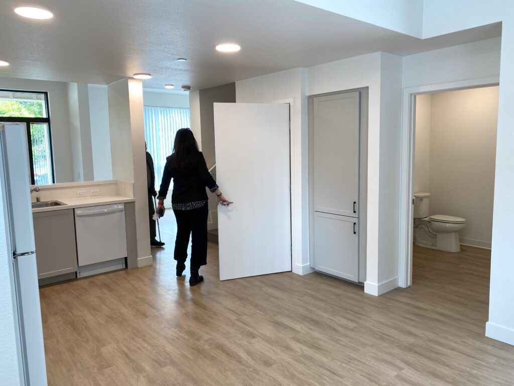 Kitchen, living room and bathroom of new townhome with wood flooring and one person opening a closet door to show another the interior